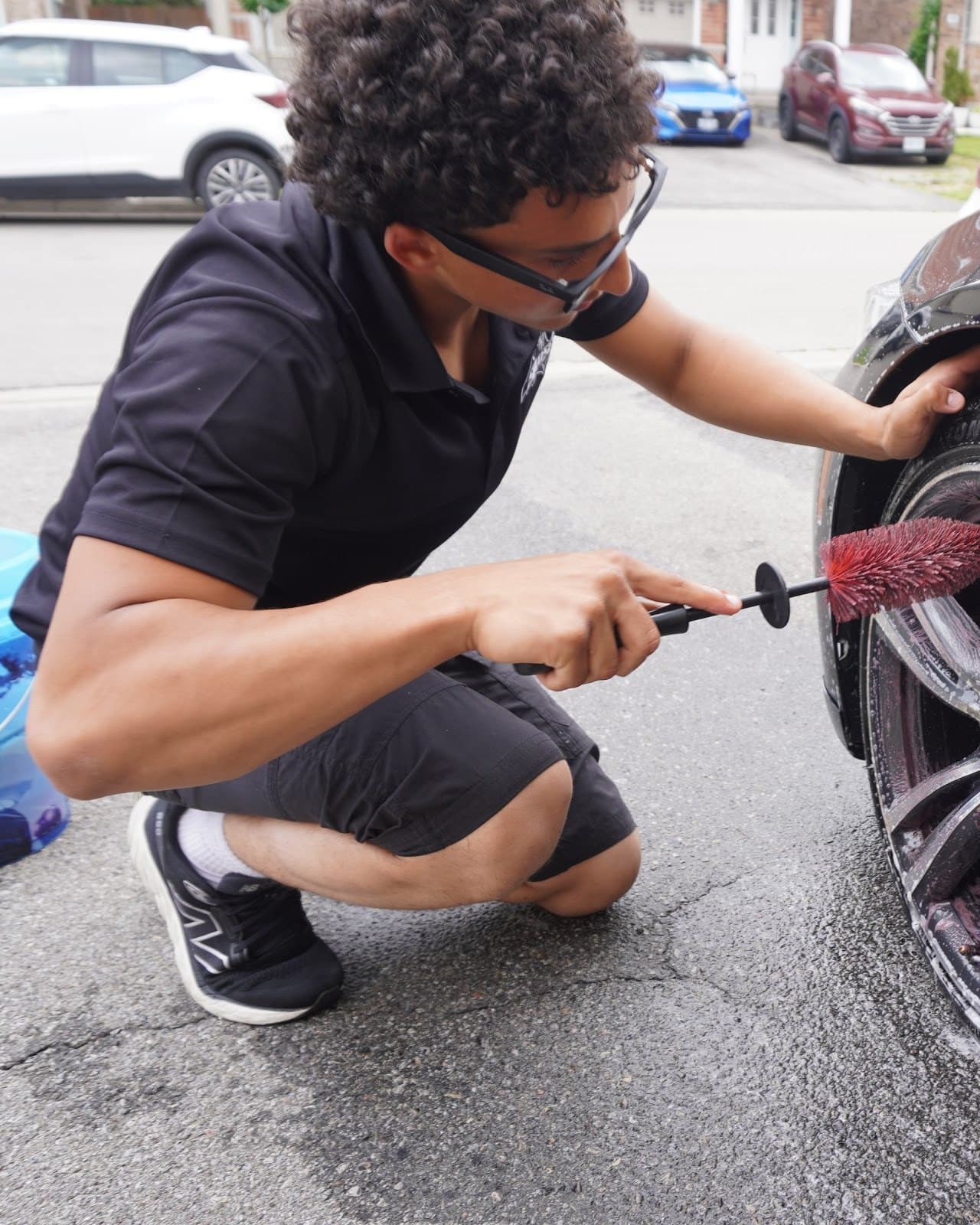 Zachariah, owner of SoloSpa, crouched at a car's front wheel cleaning the alloy with a detailing brush